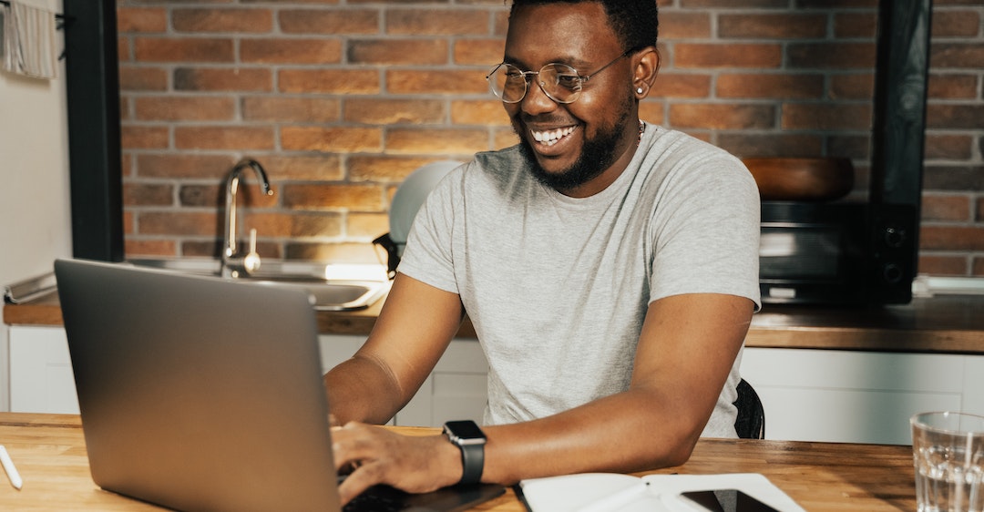 Happy black man running online background check from laptop