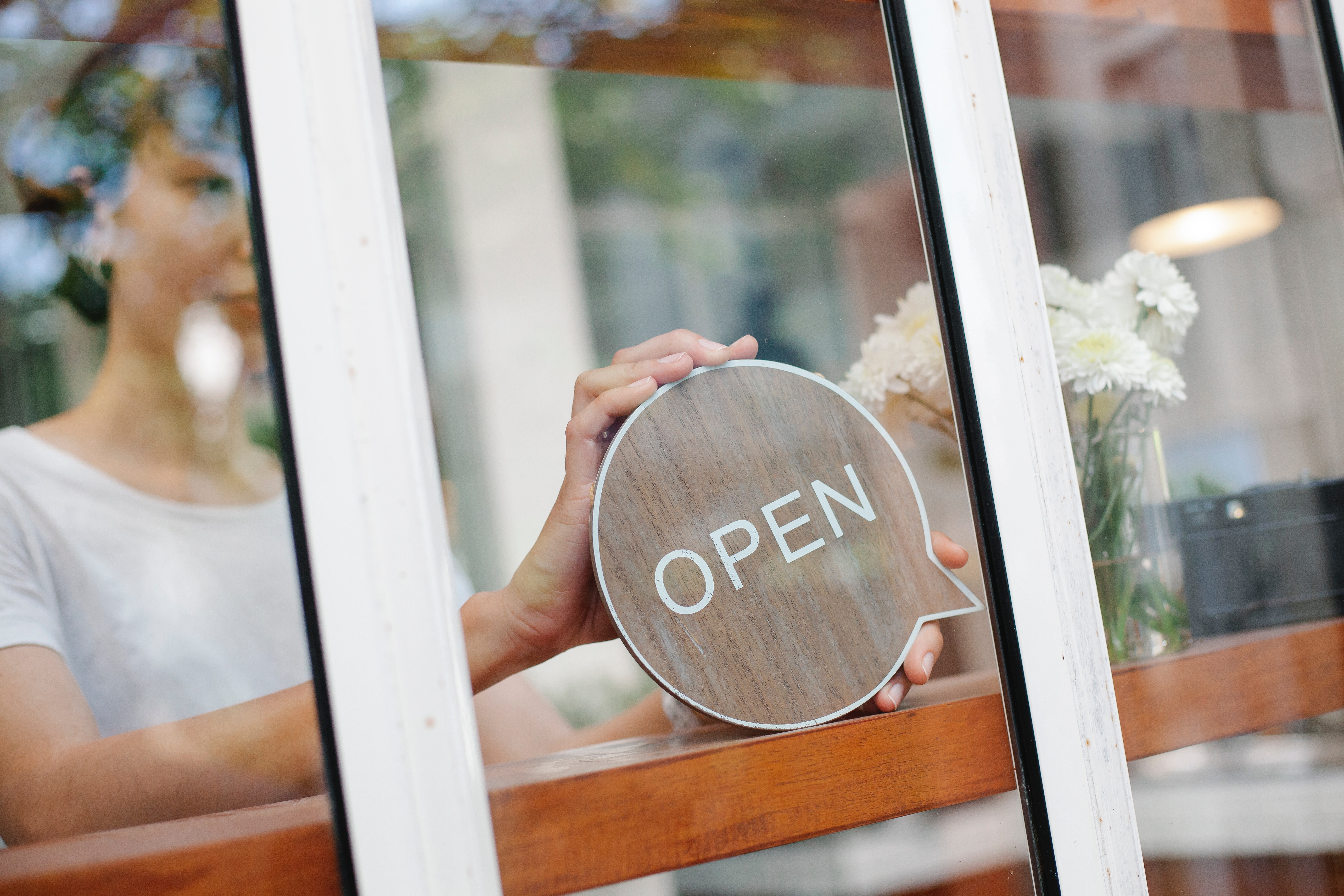 Happy white woman small business owner with open for business sign in store window